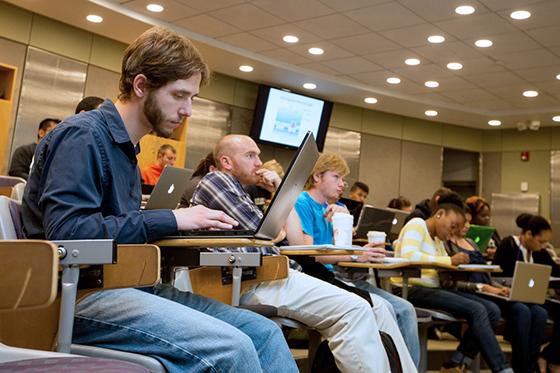 Photo of a Chatham University student sitting in a Chatham Eastside lecture hall taking notes on his laptop.