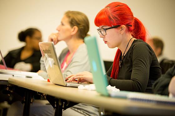 Photo of a student with glasses and bright red hair, typing on her laptop during class