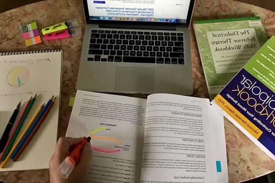 Photo from above of a student highlighting a diagram in a psychology notebook on a table filled with psychology notebooks, pens, and a laptop. 