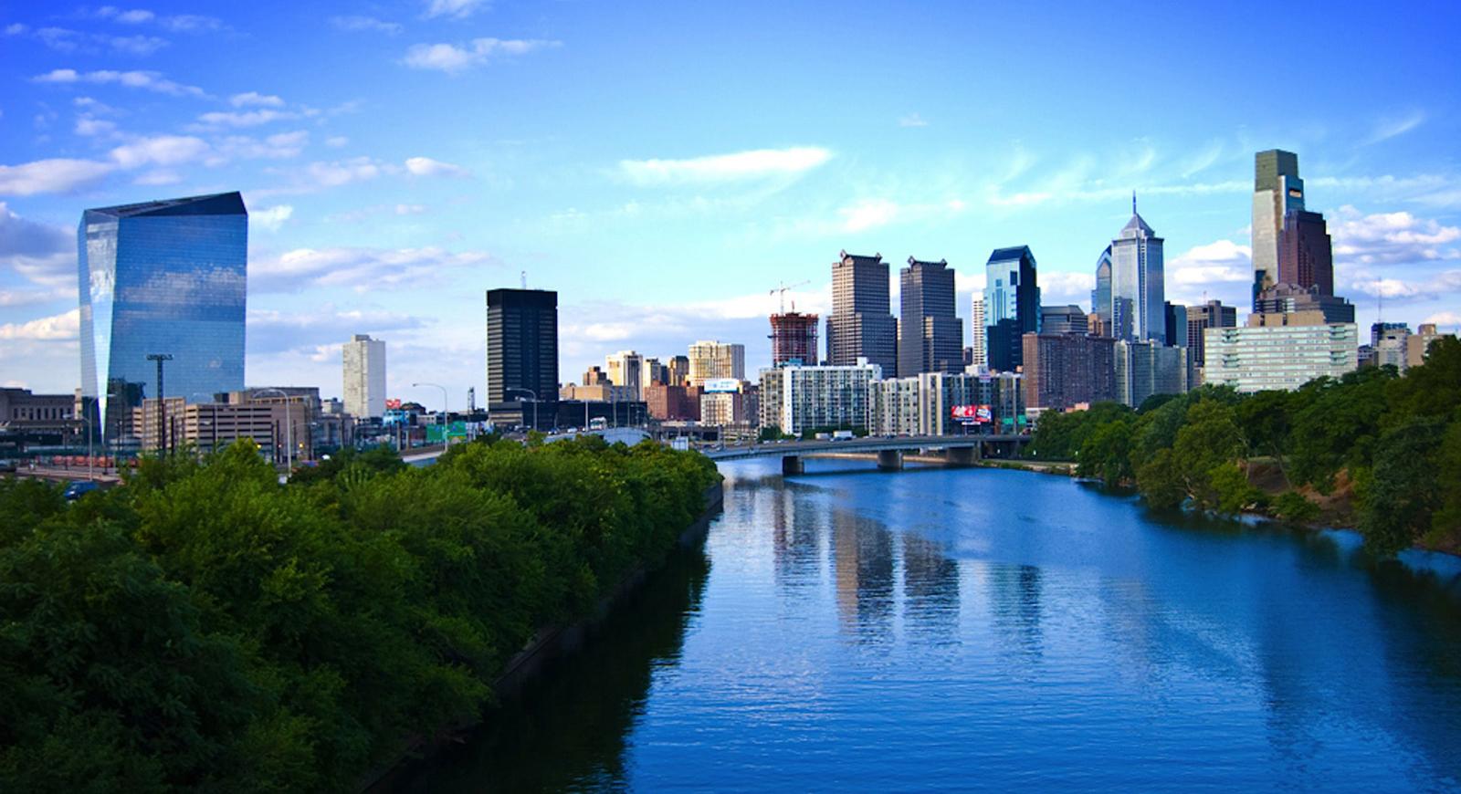 Photo of the Philadelphia skyline with a river and blue sky. 